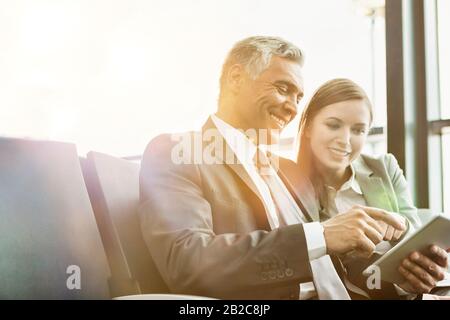 Un uomo d'affari maturo che mostra un tablet digitale a una giovane donna d'affari attraente in aeroporto Foto Stock