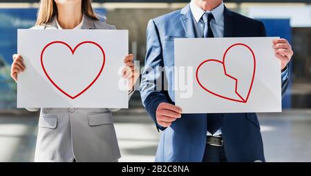 L'uomo e la donna che hanno una placida bianca con un cuore e un cuore spezzato che si disegnano sulla placarda Foto Stock