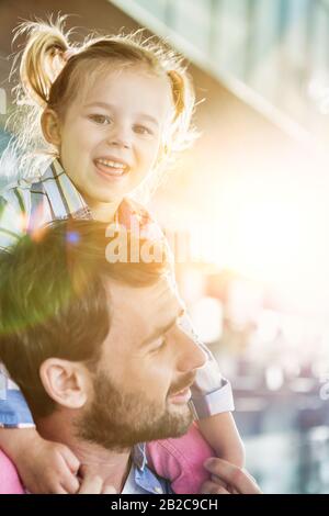 Ritratto di uomo che porta sua figlia sulla spalla in aeroporto con lente flare Foto Stock