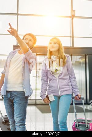 Uomo maturo che arriva con sua figlia in aeroporto alla ricerca del loro volo Foto Stock