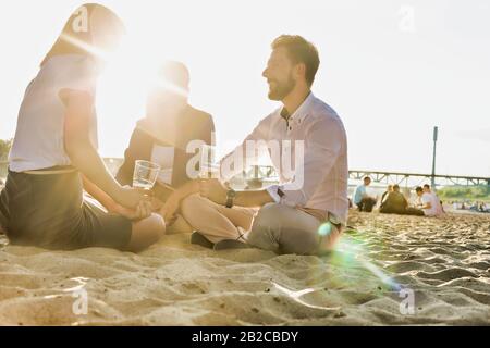 Gli uomini d'affari celebrano il successo mentre bevono birra sulla spiaggia con lenti che si ripresentano sullo sfondo Foto Stock