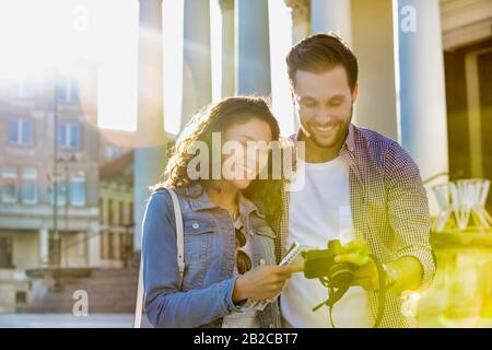 Ritratto di bel giovane uomo che mostra le immagini sulla fotocamera alla sua bella ragazza, mentre in piedi contro il museo con lente flare in background Foto Stock