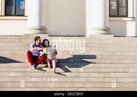 Ritratto di bel giovane uomo che mostra le immagini sulla fotocamera alla sua bella ragazza, mentre seduto contro il museo con lente flare in background Foto Stock