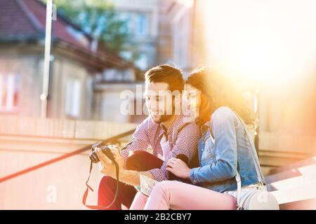Ritratto di bel giovane uomo che mostra le immagini sulla fotocamera alla sua bella ragazza, mentre seduto contro il museo con lente flare in background Foto Stock