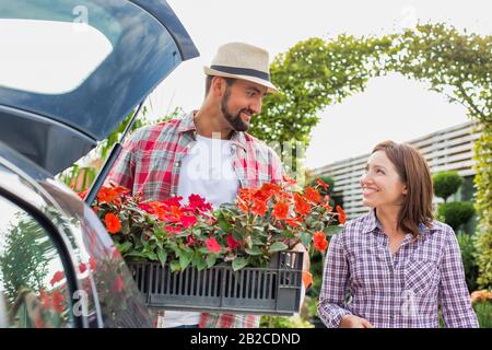 Ritratto di giardiniere maturo che mette i fiori sulla cassa in tronco di automobile mentre parla con la donna nel negozio del giardino Foto Stock