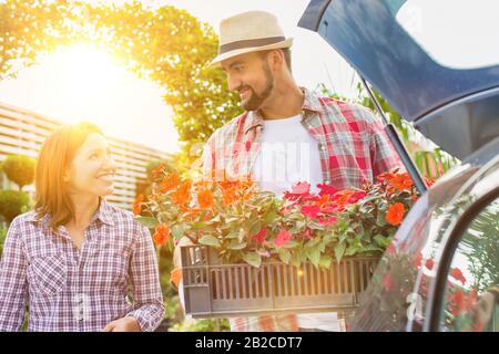 Ritratto di giardiniere maturo che mette fiori sul tronco dell'automobile mentre parla con la donna nel negozio del giardino Foto Stock