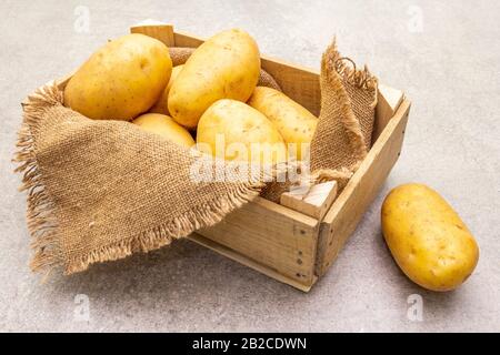 Patate crude giovani non pelate in cassa di legno. Nuovo raccolto, su sacco, pietra sfondo, copia spazio Foto Stock