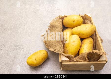 Patate crude giovani non pelate in cassa di legno. Nuovo raccolto, su sacco, pietra sfondo, copia spazio Foto Stock