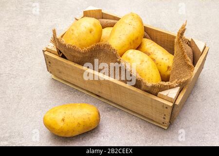 Patate crude giovani non pelate in cassa di legno. Nuovo raccolto, su sacco, fondo di pietra, primo piano Foto Stock