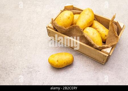 Patate crude giovani non pelate in cassa di legno. Nuovo raccolto, su sacco, pietra sfondo, copia spazio Foto Stock