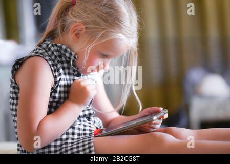 Bambina in un abito seduto guardando un video e giocando su uno smartphone. Foto Stock
