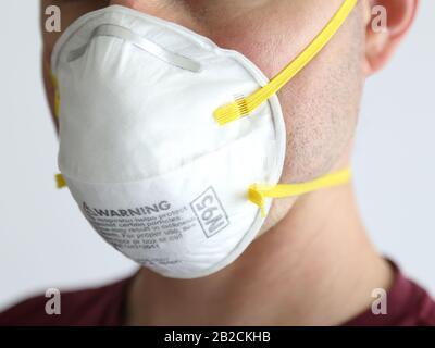 Un uomo è mostrato indossare una maschera protettiva N95 bianco crepuscolo da vicino, impostato su uno sfondo bianco durante il giorno. Foto Stock