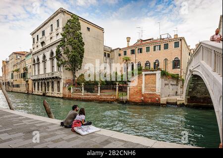 Venezia, Italia. Coppia Romainic seduto sul marciapiede del canale vicino al ponte nella parte storica della città Foto Stock
