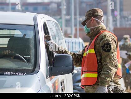 Un soldato statunitense scherma i passeggeri per il COVID-19, utilizzando un termometro presso un cancello d'ingresso per i militari della Garrison Humphreys, 27 febbraio 2020 a Pyeongtaek, Corea del Sud. Lo scoppio del nuovo coronavirus nella Corea del Sud è secondo solo alla Cina. Foto Stock