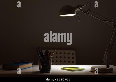 Luogo Di Lavoro. La lampada al buio con la luce accesa, si illumina sul tavolo. Foto Stock