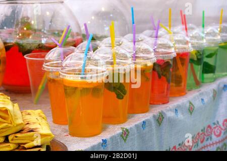 Bevande estive luminose con fette di limone, menta e acqua frizzante in tazza di plastica con paglia. Street food e cucina all'aperto. Foto Stock