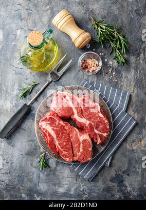 Due fresche Raw Meat prime Black Angus Chuck roll bistecca su un tagliere in legno su uno sfondo grigio. Vista dall'alto. Foto Stock