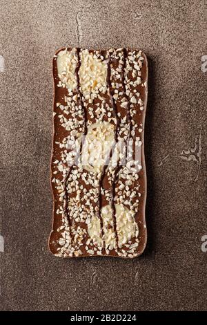 Vista dall'alto della barra di cioccolato composta da tre tipi di cioccolato e nocciole schiacciate su sfondo marrone Foto Stock