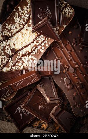 Vista dall'alto di fette di cioccolato fondente e al latte con gocce di cioccolato su sfondo marrone Foto Stock