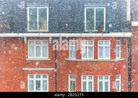 Neve pesante che cade a Londra con un palazzo in mattoni rossi sullo sfondo Foto Stock