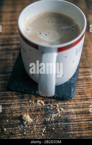 Tazza di caffè lattiginoso e briciole di biscotto su un tavolo di legno Foto Stock