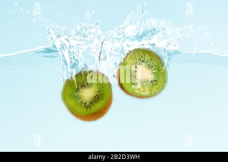 I kiwi freschi cadono in acqua limpida con spruzzi su sfondo blu Foto Stock