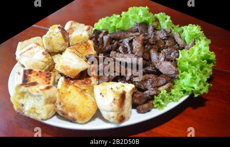 Porzione di carne alla griglia sul piatto con salsa di prezzemolo e pane. Piatto del ristorante. Foto isolata su sfondo nero. Foto Stock