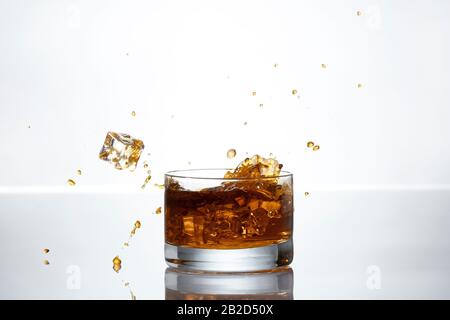 Un cubetto di ghiaccio si tuffa in un bicchiere di whisky Foto Stock