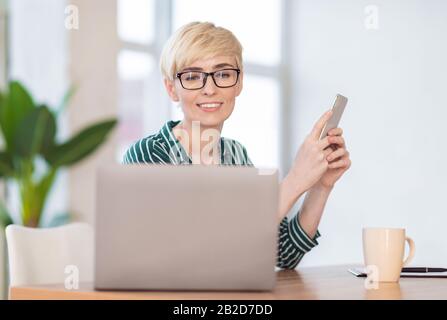 Businesswoman Allegro Che Usa L'Applicazione Del Telefono Mobile Seduta In Ufficio Foto Stock