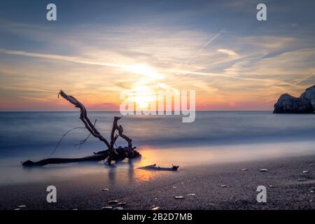 Incredibile tramonto sull'isola di Milos. Ramo su spiaggia sabbiosa e soft surf Egeo mare. Grandi rocce di pietra in acqua. Serata tranquilla paesaggio mediterraneo Foto Stock