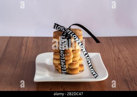 Nelle immagini, biscotti appena sfornati di frollino legati con un nastro nero su un tavolo di legno Foto Stock