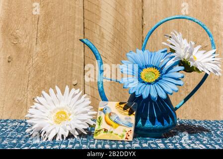 Luminoso tramonto disposizione di fiori di tessuto, uccello di ceramica in un waterpot di metallo blu con sfondo di legno. CopySpace per il tuo messaggio/annuncio Foto Stock