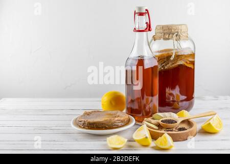 Kombucha superfood pro biotic tè fungo bevanda in bottiglia di vetro e vaso con limone, zenzero, tè su sfondo bianco. Copia spazio Foto Stock