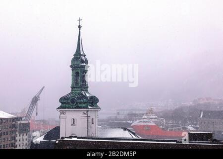 Inverno A Bergen, Norvegia. Nevicando alla chiesa di Nykirken. Vista verso il porto di Vaagen, Bergenhus e Sandviken. Foto Stock