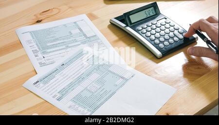 Primo piano del modulo fiscale USA 1040 e carta per il calcolo e il riempimento manuale con calcolatrice in ufficio. Foto Stock