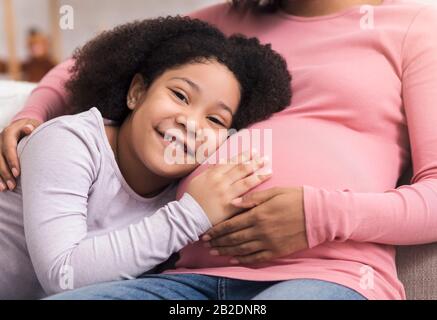 Pulcini Del Bambino. Piccola Figlia Graziosa Che Ascolta Il Ventre Della Madre Incinta Foto Stock