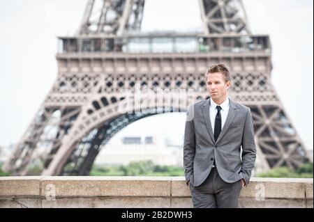 Serio uomo d'affari europeo che si trova da solo di fronte alla Torre Eiffel di Parigi, in Francia Foto Stock