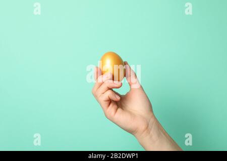 La mano femmina tiene l'uovo dorato sullo sfondo della menta, lo spazio per il testo Foto Stock