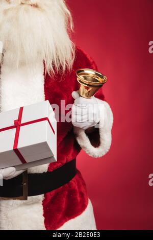 immagine ritagliata di babbo natale che tiene la campana presente e che suona su sfondo rosso Foto Stock