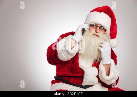 babbo natale che parla al telefono si affaccia su sfondo grigio Foto Stock