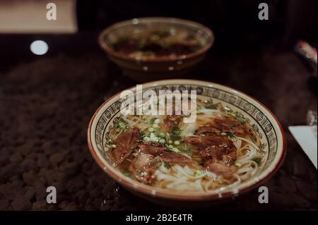 Un grande piatto di zuppa vietnamita calda pho bo su un tavolo scuro, sullo sfondo un altro piatto di zuppa Foto Stock