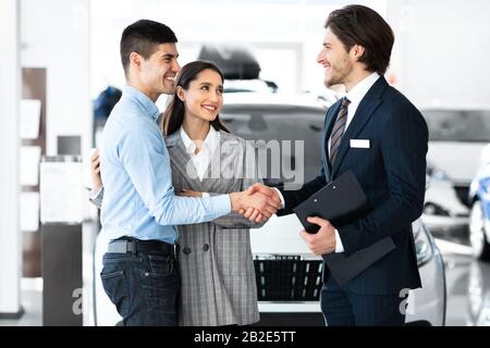 Uomo Che Si Stringe Le Mani Con Il Responsabile Delle Vendite Di Auto Nel Dealership Store Foto Stock