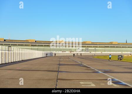 Le persone che praticano sport su un ex campo di atterraggio e sullo sfondo del precedente edificio del terminal aeroportuale a Tempelhof Park, ex aeroporto militare, a Berlino. Foto Stock