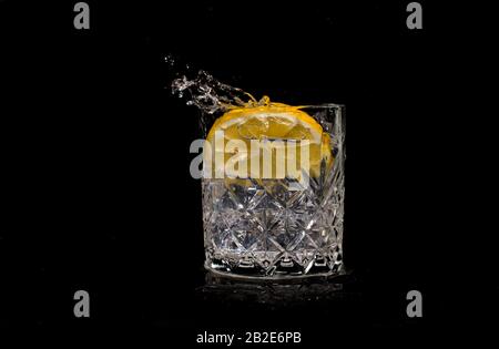 acqua potabile acqua con limone soda versamenti quando il ghiaccio è gettato con gocce su uno sfondo nero Foto Stock