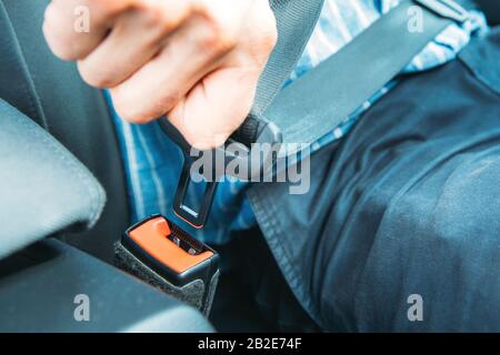 Primo piano del conducente seduto sul sedile dell'auto e allacciare/indossare la cintura di sicurezza. Sicurezza, trasporto, concetto di viaggio sicuro. Foto Stock