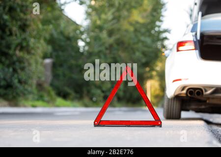 Primo piano del simbolo del triangolo segnaletico rosso e della vettura bianca rotta su strada, copia spazio. Foto Stock