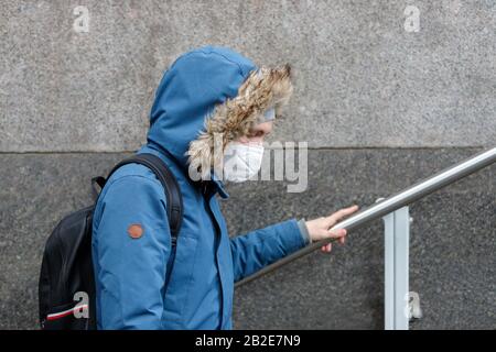 Malato con una cappa che indossa maschera facciale protettiva contro le malattie infettive trasmissibili e come protezione contro l'influenza o il coronavirus in publ Foto Stock