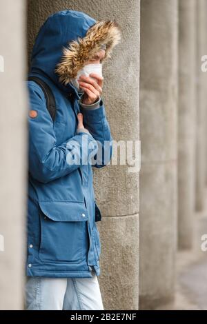 Uomo malsano con un cappuccio che indossa maschera facciale protettiva all'aperto, copre la bocca dalla tosse polmonare. Influenza, infezioni respiratorie, polmonite, bronc Foto Stock