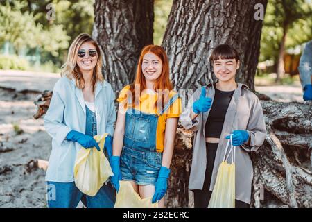 Amici che raccolgono rifiuti dal parco. Le ragazze mostrano il pollice in su. Foto Stock