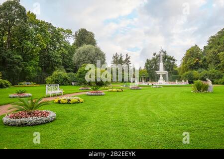 Un tranquillo giardino con fiori, fontana d'acqua e panca vicino al Giardino e Palazzo di Caterina a Pushkin, San Pietroburgo, Russia. Foto Stock
